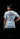 A woman shown from the back wearing a light blue short-sleeve t-shirt with a large black graphic print on the back. The graphic features a snake wrapped around a cross and the words 'PASSION IS PROCESSED' with 'SCC' in the center.